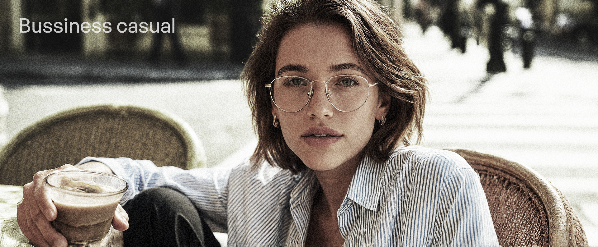 Woman sitting outdoors holding a cup, wearing glasses and a light shirt.