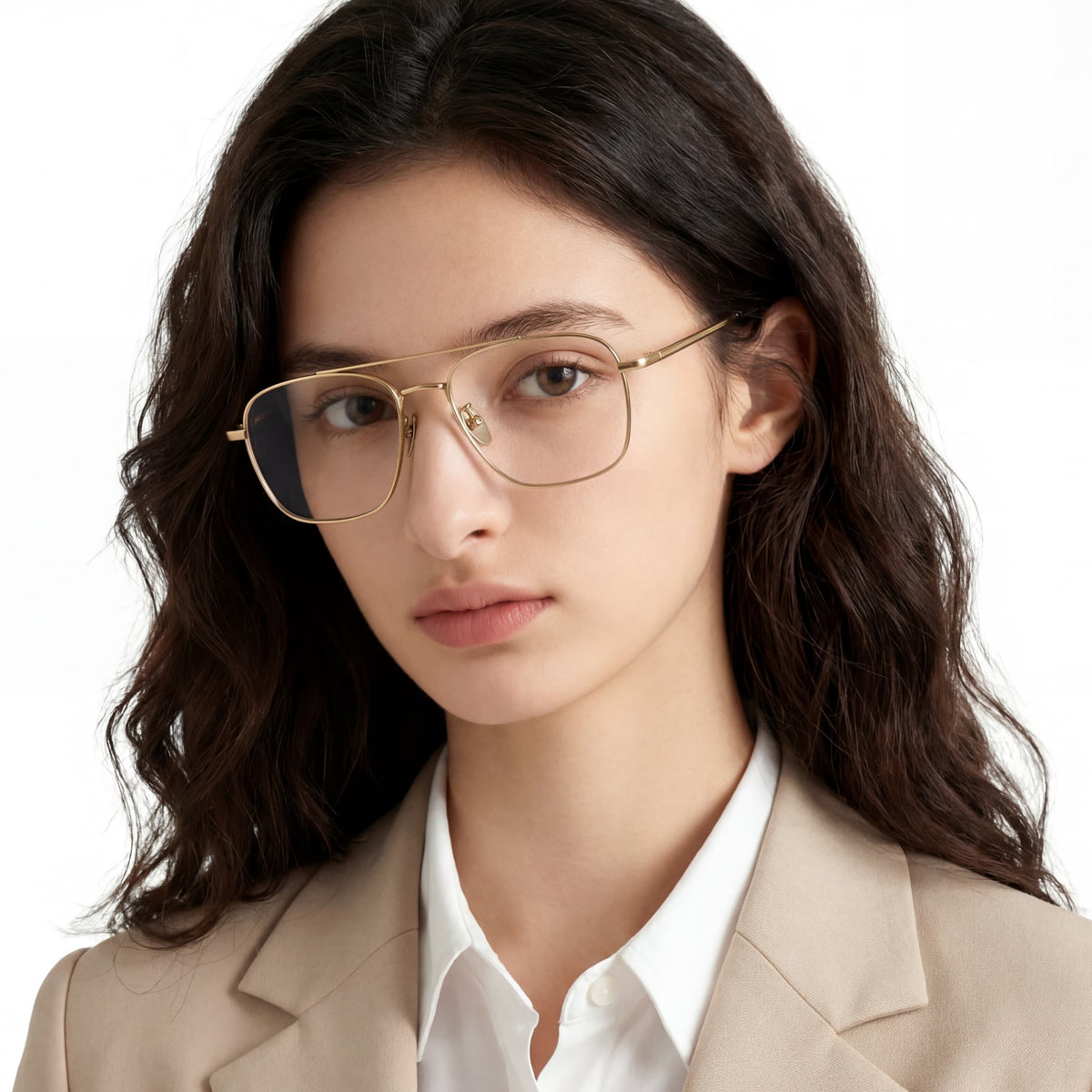 Woman wearing gold-framed glasses and a beige blazer on a white background