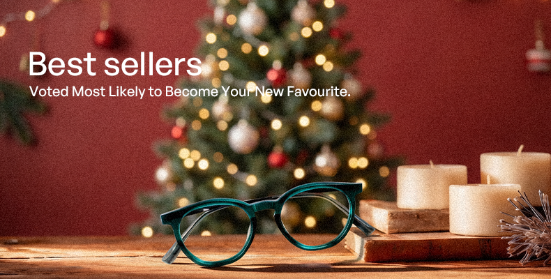 Green eyeglasses on a wooden surface with a Christmas tree and candles in the background.