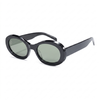 Oval sunglasses with a glossy black frame and muted green-gray tinted lenses, shown at a three-quarter angle on a plain white background.