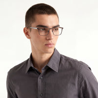 Man wearing glasses and a gray shirt against a white background