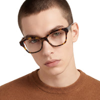 Person wearing tortoiseshell glasses with a plain background