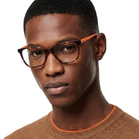 Man wearing glasses and a brown sweater with orange accents on a white background