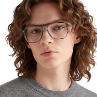 Person with curly hair wearing glasses and a gray sweater on a white background