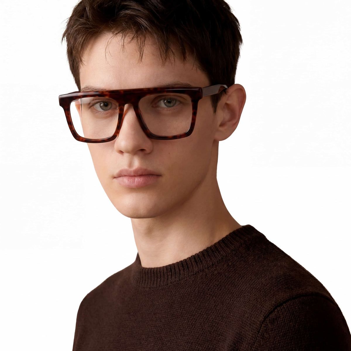 Person wearing tortoiseshell glasses and a brown sweater on a white background