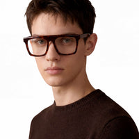 Person wearing tortoiseshell glasses and a brown sweater on a white background