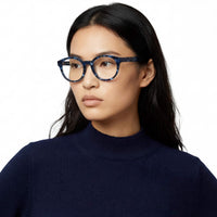 Woman wearing blue tortoiseshell glasses against a white background