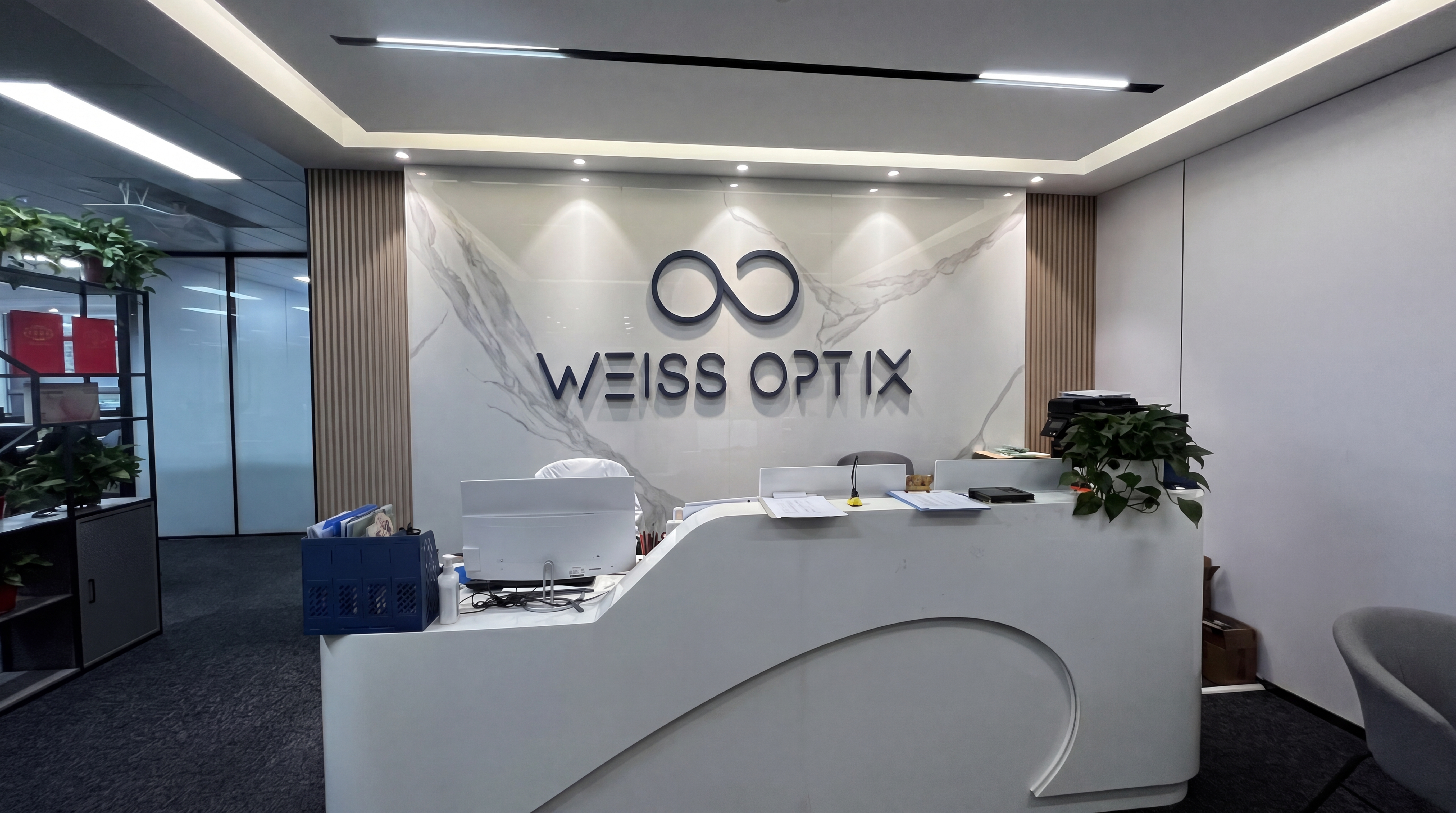 WEISS OPTIX brand office reception front desk interior photo with marble logo wall and green plants