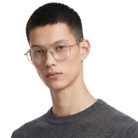 Person wearing gold-framed glasses and a gray sweater on a white background