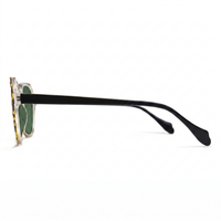 Side profile of a pair of sunglasses with a clear acetate frame featuring a gold tortoiseshell pattern, green lenses, and black temple arms, shown on a white background.