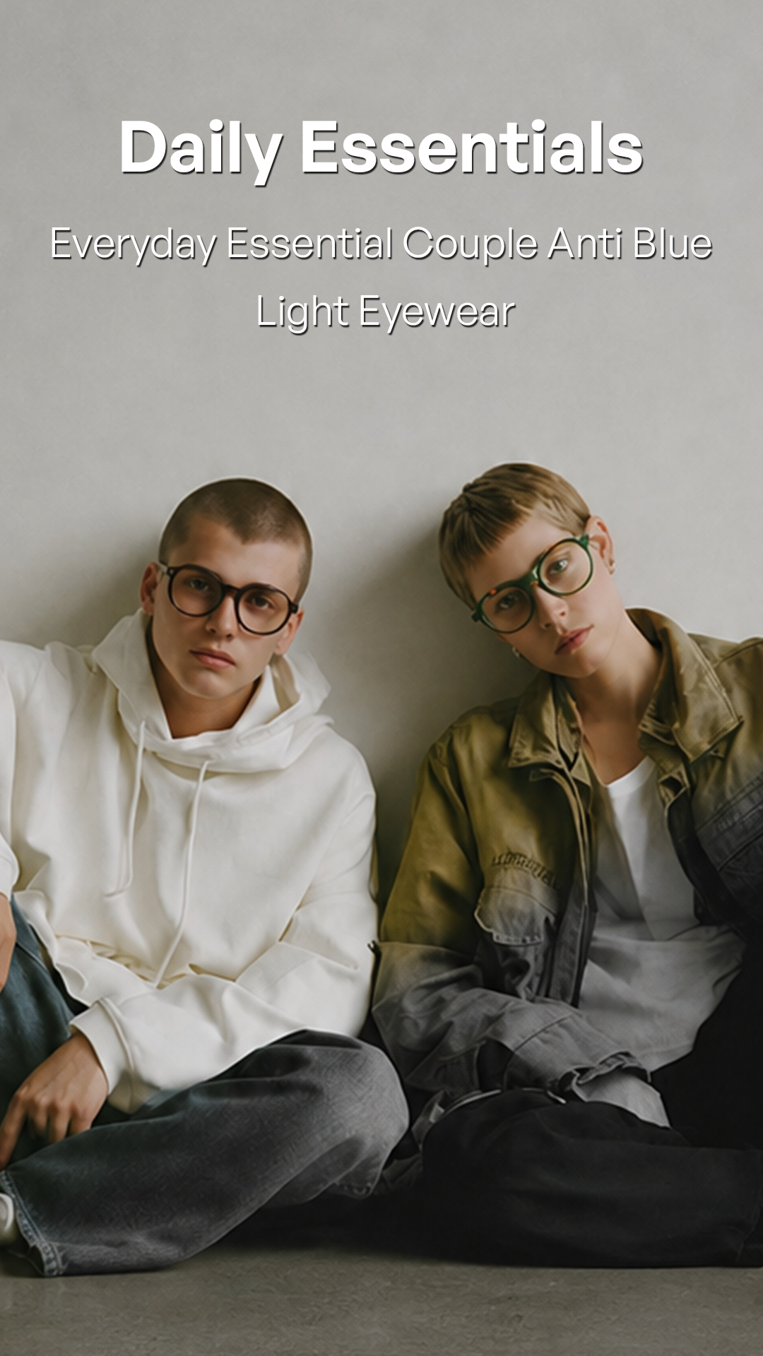 Two models wearing light blue anti-blue light eyeglasses, sitting against a neutral gray wall. The text overlay at the top reads 'Daily Essentials Everyday Essential Couple Anti Blue Light Eyewear'.