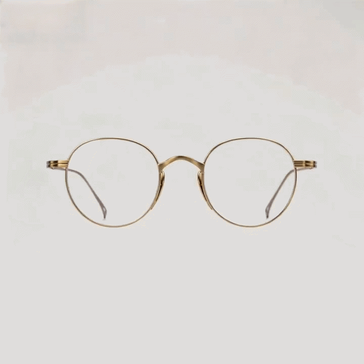 Light gold metal round eyeglasses frame, side profile shot on light gray studio background